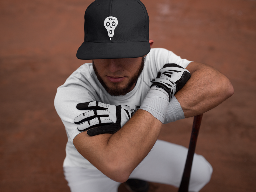 Squatting batter wearing a black rapper baseball cap in black with a white Lazybones Clothing skull logo